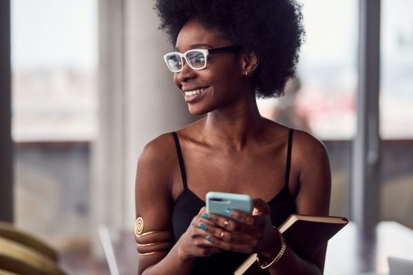 Cheerful african american woman holding smartphone and notepad